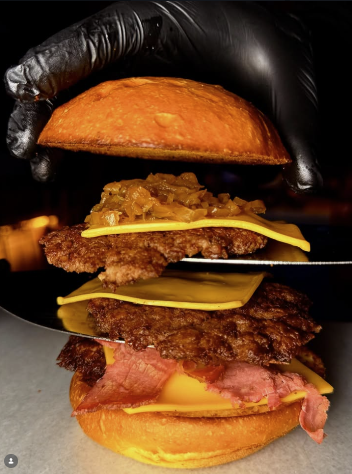 Siyah eldivenle tutulan, katmanları açılmış SmashLab burger